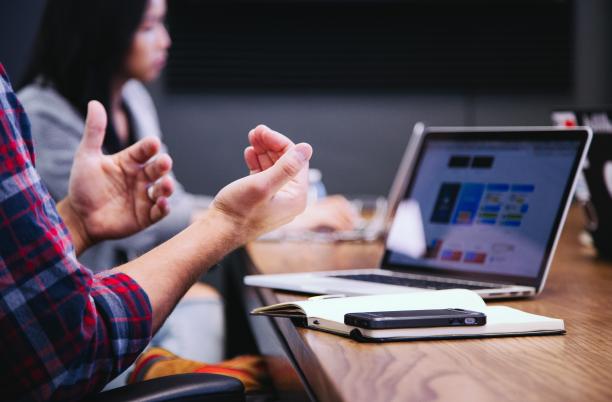 A stock photo showing someone talking at a meeting with a PC in front of them