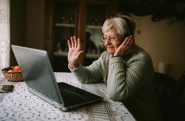 Woman with headphones on sitting at a computer waving at the screen