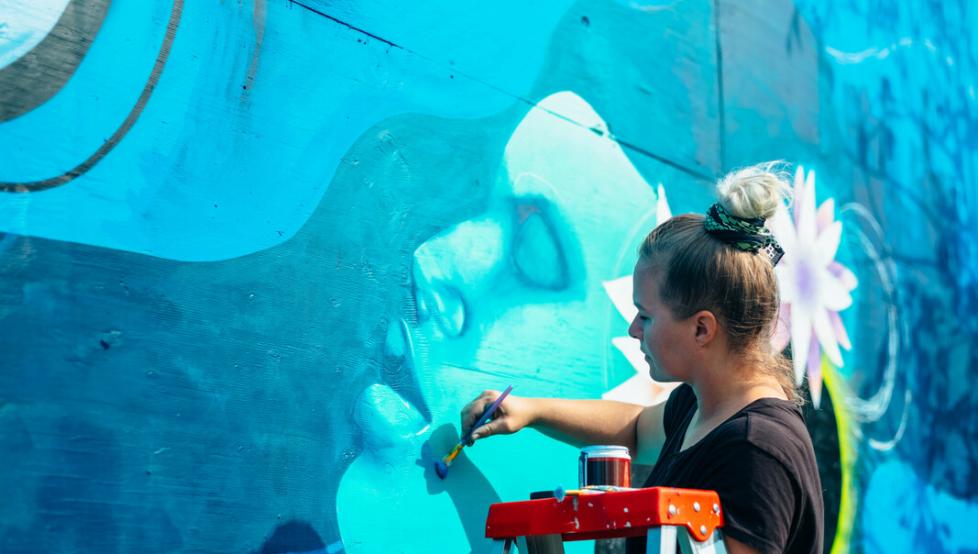 A female artist paints on a wall mural