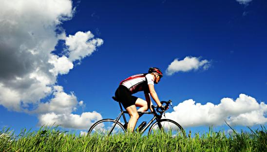A stock photo of someone cycling on a sunny day with a few white clouds